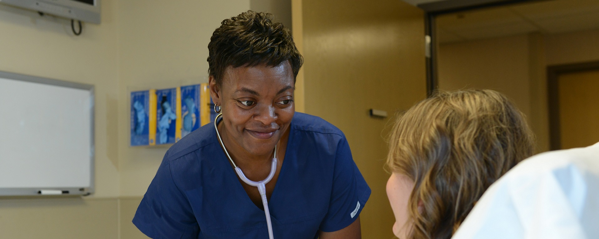 A smiling black nurse bending over to help a patient in bed.